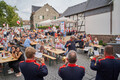 Im Vordergrund spielen Mitglieder der Wiener Neustädter Stadtkapelle. Im Hintergrund sitzen Menschen an Biertischgarnituren. Die Umgebung ist mit rot-weißen Luftballons und Girlanden geschmückt. 